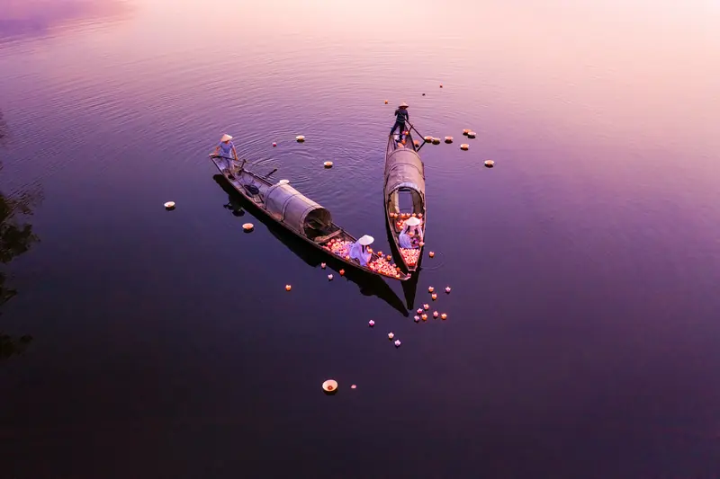 Due barche di legno sul fiume a Hoi An al crepuscolo, con lanterne di carta che galleggiano sull'acqua